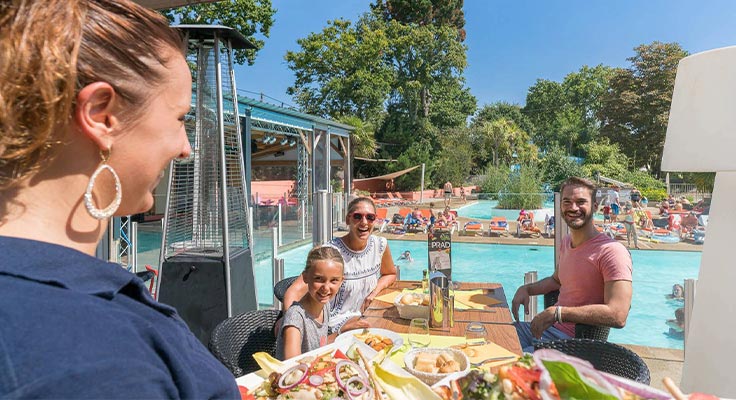 Serveuse apportant les plats d'une famille sur la terrasse du restaurant du camping Le Port de Plaisance à Bénodet en Bretagne